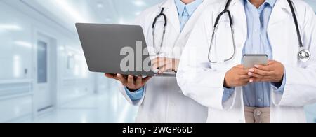 In a brightly lit hospital hallway, two medical professionals engage in digital healthcare Stock Photo