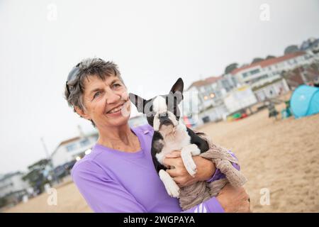Portrait of a senior woman smilingat the beach with her dog, a Boston terrier Stock Photo