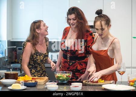 A mixed group of female friends having fun and laughing whist preparing party food in a modern kitchen Stock Photo