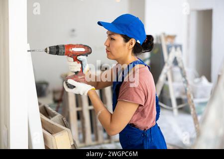 Woman builder using drill to bore hole in wall Stock Photo