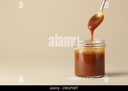 Taking tasty salted caramel with spoon from jar on pale yellow background, space for text Stock Photo