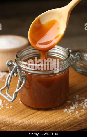 Taking tasty salted caramel with spoon from jar on table, closeup Stock Photo