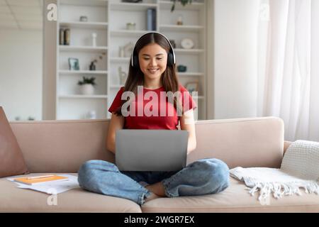 Distance Learning. Young Asian Woman In Headphones Studying With Laptop At Home Stock Photo