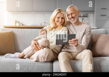 Positive beautiful loving senior spouses using digital tablet at home Stock Photo