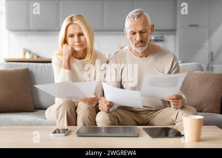 Worried Senior Spouses Reading Papers And Bills At Home Stock Photo