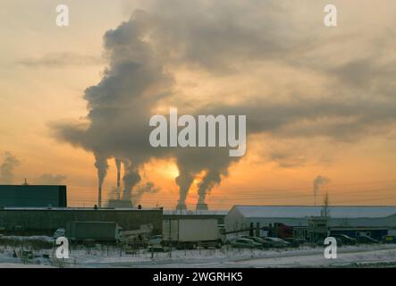 The smoke from the CHP chimneys blocked the sun in the evening sky at sunset. In the foreground is a parking lot with a white truck on it Stock Photo