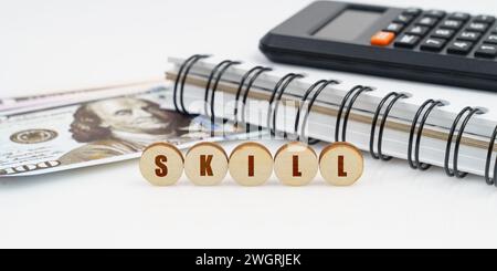 Business and finance concept. On a high surface lie a notepad, a calculator, dollars and wooden circles with the inscription - SKILL Stock Photo