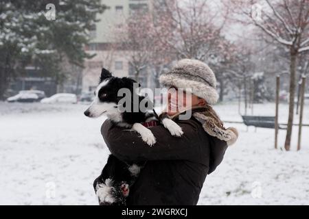 Blonde woman dressed for winter with furry hat and scarf, playing with her dog, Milano, Italy Stock Photo