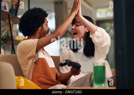 Young enthusiastic couple giving each other high five while sitting on couch at home and playing new video game together Stock Photo