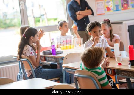 Male teacher sitting with his students in class at break time while they have lunch Stock Photo