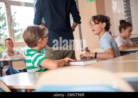 Two young boys in class talking behind teachers back Stock Photo
