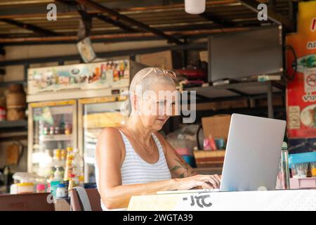 Mid aged woman solo traveller working on her laptop in a local restaurant in Chiang Mai. Thailand. Stock Photo