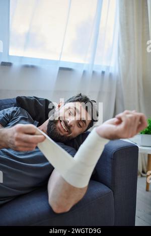 ill man with smile and bandage on arm after attempting suicide on sofa, mental health awareness Stock Photo