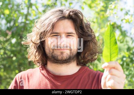 young man with a leaf in the hand before green bushes climate protection Stock Photo