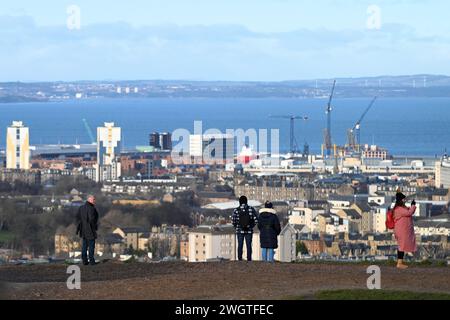 Edinburgh, Scotland, UK. 6th February 2024. Visitors on Calton hill wrapped up against the cold blustery wind and changeable weather conditions with views across the city rooftops looking north over the Forth estuary to Fife. Credit: Craig Brown/Alamy Live News Stock Photo