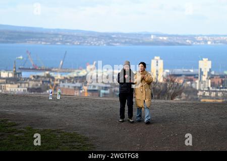 Edinburgh, Scotland, UK. 6th February 2024. Visitors on Calton hill wrapped up against the cold blustery wind and changeable weather conditions with views across the city rooftops looking north over the Forth estuary to Fife. Credit: Craig Brown/Alamy Live News Stock Photo