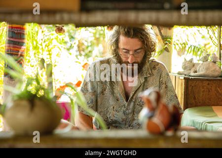 Young Man works on his laptop and phone in a restaurant in Northern Thailand, He is a digital Nomad working remotely. Stock Photo