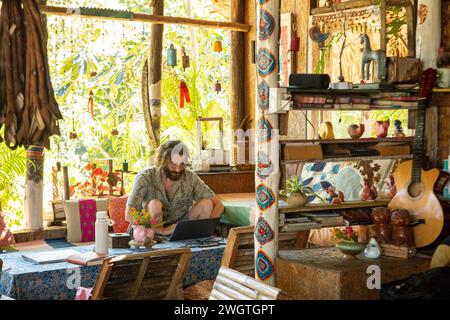 Young Man works on his laptop and phone in a restaurant in Northern Thailand, He is a digital Nomad working remotely. Stock Photo