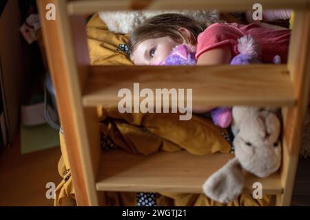 young girl laying on her bed surrounded by her teddies and hugging Stock Photo