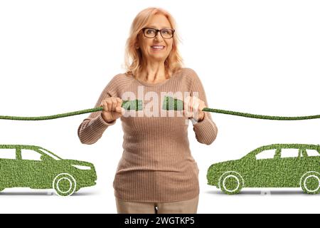 Happy mature woman plugging in green electric cables for electric vehicles isolated on white background Stock Photo