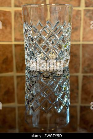 A small crystal whisky tumbler standing on a dark reflective surface. Stock Photo