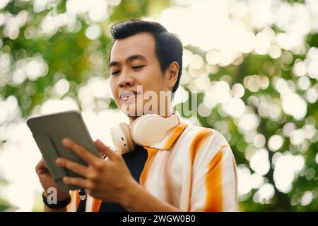 Young man with tablet looking at screen while communicating in video chat or watching online video in natural environment Stock Photo