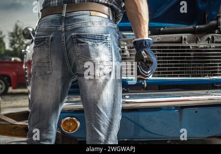 Caucasian Man Working on His Classic Car. Keeping Iron Wrench in His Hands Close Up. Stock Photo