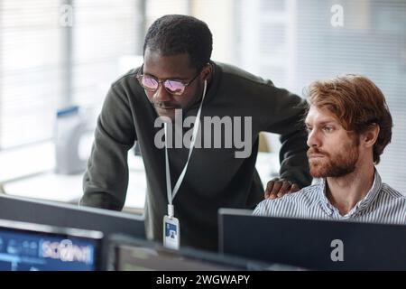 Portrait of young Black man mentoring bearded IT developer and reviewing code looking at computer screen in office Stock Photo
