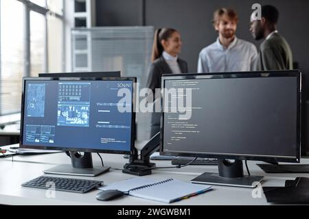 PC computers with code lines and blue data on screen at desk in cybersecurity company with diverse team in blurred background copy space Stock Photo