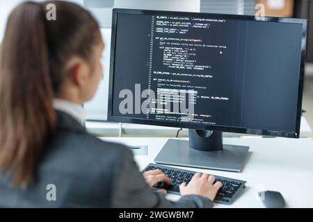 Over shoulder view of female programmer using computer with code lines on screen in IT company office copy space Stock Photo