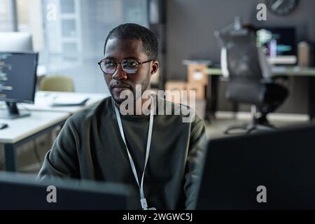 Minimal portrait of focused Black man using computer in IT development office with code lines reflection in glasses copy space Stock Photo