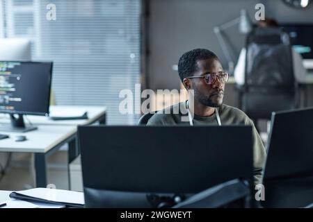 Portrait of Black young man wearing glasses as IT programmer using computer and reviewing data in office copy space Stock Photo