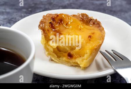 One uneaten Pastel de nata or Portuguese egg dessert on a white plate. Pastel de Belm is a small pie with a crispy puff pastry crust and a custard cre Stock Photo