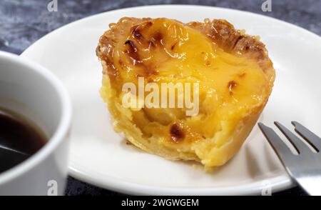 One Pastel de nata or Portuguese egg tart on a white plate. Pastel de Belm is a small pie with a crispy puff pastry crust and a custard cream filling Stock Photo