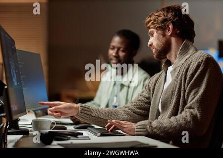 Side view portrait of bearded man pointing at computer screen and talking to colleague while reviewing data in office, copy space Stock Photo