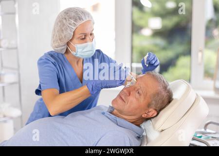 Old man having face care by means of injection in aesthetic clinic Stock Photo