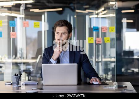Focused mature businessman working intently in a modern office with sticky notes on glass. Concept of leadership and professionalism. Stock Photo