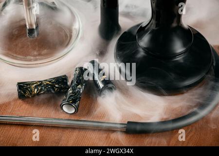 Two hookahs on a brown wooden background. Artistic shooting with white smoke. Stock Photo