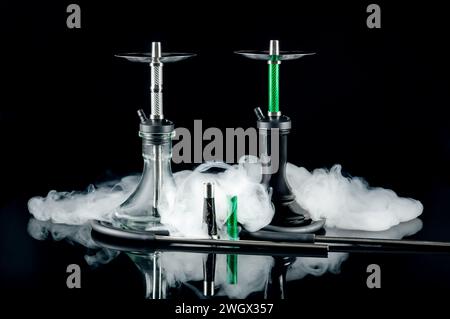 Two hookahs with white puffs of smoke on a black mirror background. Artistic shooting in a studio. Stock Photo