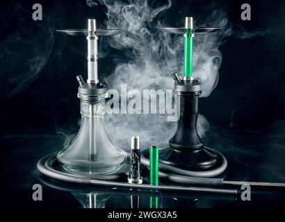 Two modern hookahs with smoke on a black mirror background. Stock Photo