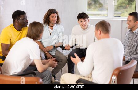 Cheerful male colleagues friendly talking sitting in circle on chairs Stock Photo