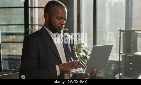African American multiethnic businessman employee professional manager using laptop typing email on keyboard focused man search digital data standing Stock Photo