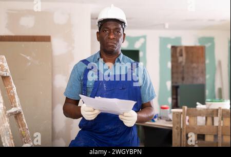 Dissatisfied african-american man construction worker holding document in hand while standing in building site Stock Photo