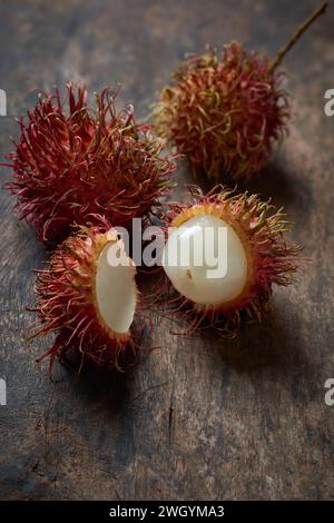 close-up of ripe rambutan, peeled and whole juicy tropical fruit native to southeast asia, scattered on wooden table top, soft focus with copy space Stock Photo
