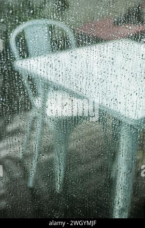 Rainy days on a terrace with metal furniture seen through a wet window Stock Photo