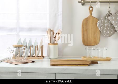 Wooden cutting boards, other cooking utensils and dishware on white countertop in kitchen Stock Photo