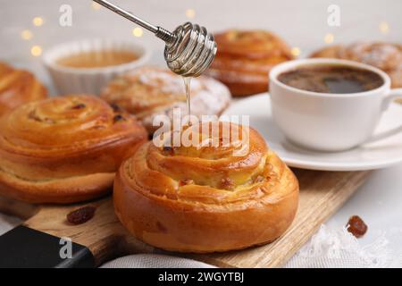 Pouring honey onto delicious rolls with raisins at table, closeup ...