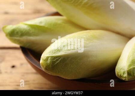 Fresh raw Belgian endives (chicory) in bowl on wooden table, closeup Stock Photo