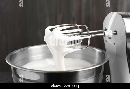 Bowl with whipped cream and hand mixer on black background, closeup Stock Photo