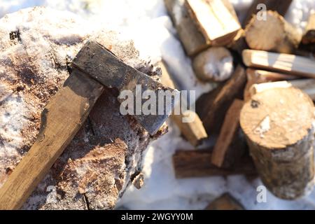 Metal axe on wooden log and pile of wood outdoors on sunny winter day, top view. Space for text Stock Photo